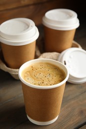 Photo of Takeaway paper coffee cups with plastic lids and cardboard holder on wooden table