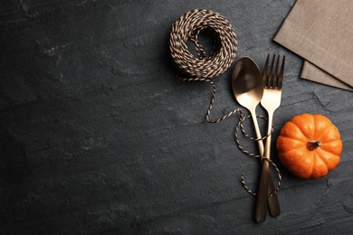 Photo of Cutlery, pumpkin and rope on black slate background, flat lay with space for text. Table setting elements