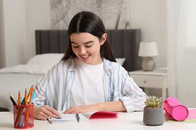 Photo of Teenage girl erasing mistake in her notebook at white desk indoors