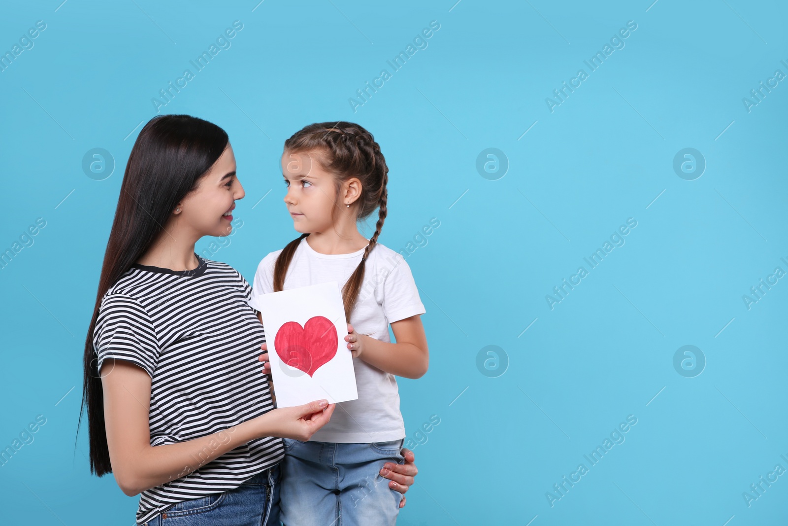 Photo of Happy woman with her cute daughter and handmade greeting card on light blue background, space for text. Mother's day celebration