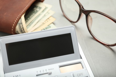 Photo of Calculator, glasses and wallet with money on grey table, closeup. Tax accounting