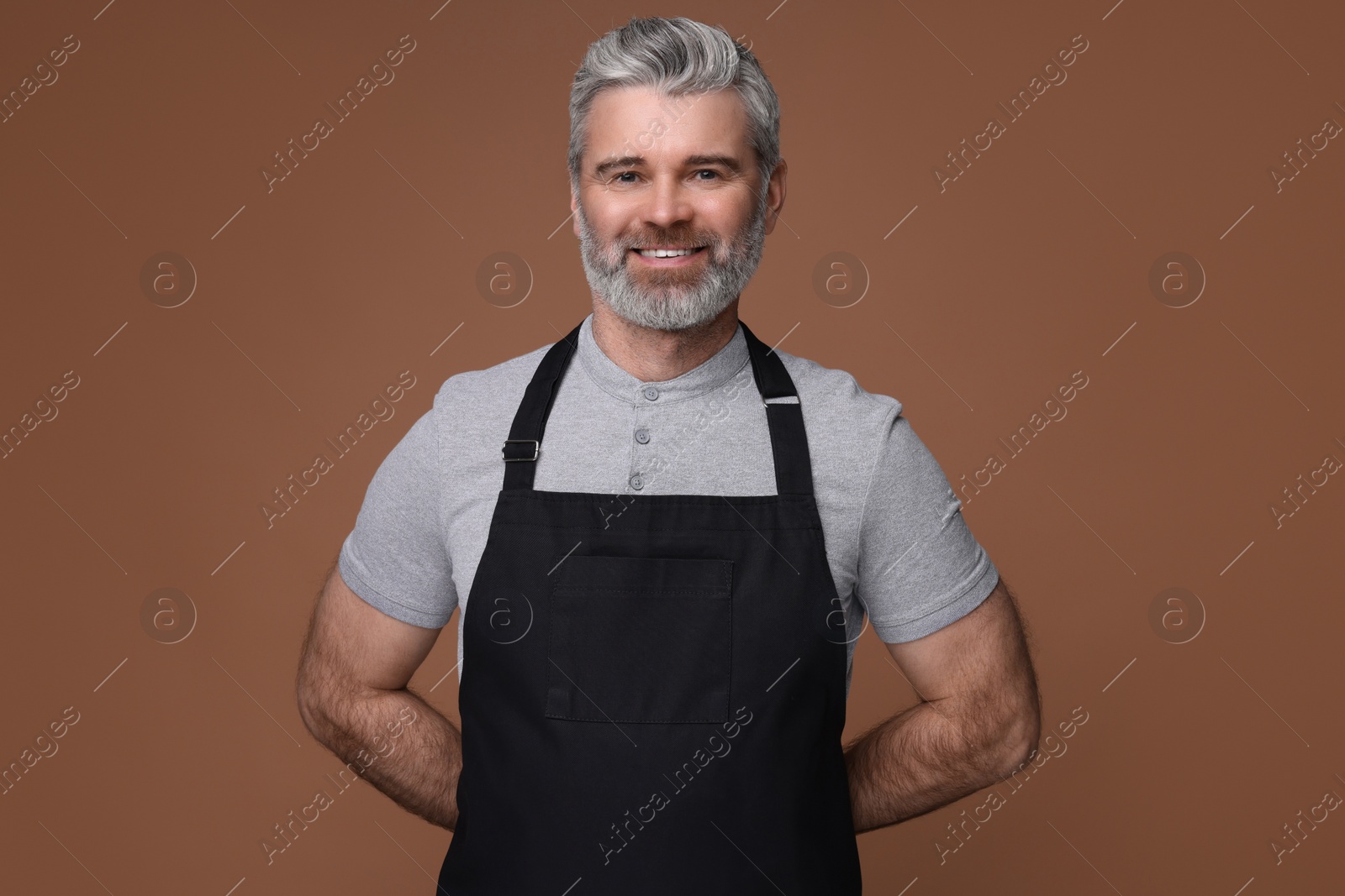 Photo of Happy man wearing kitchen apron on brown background. Mockup for design