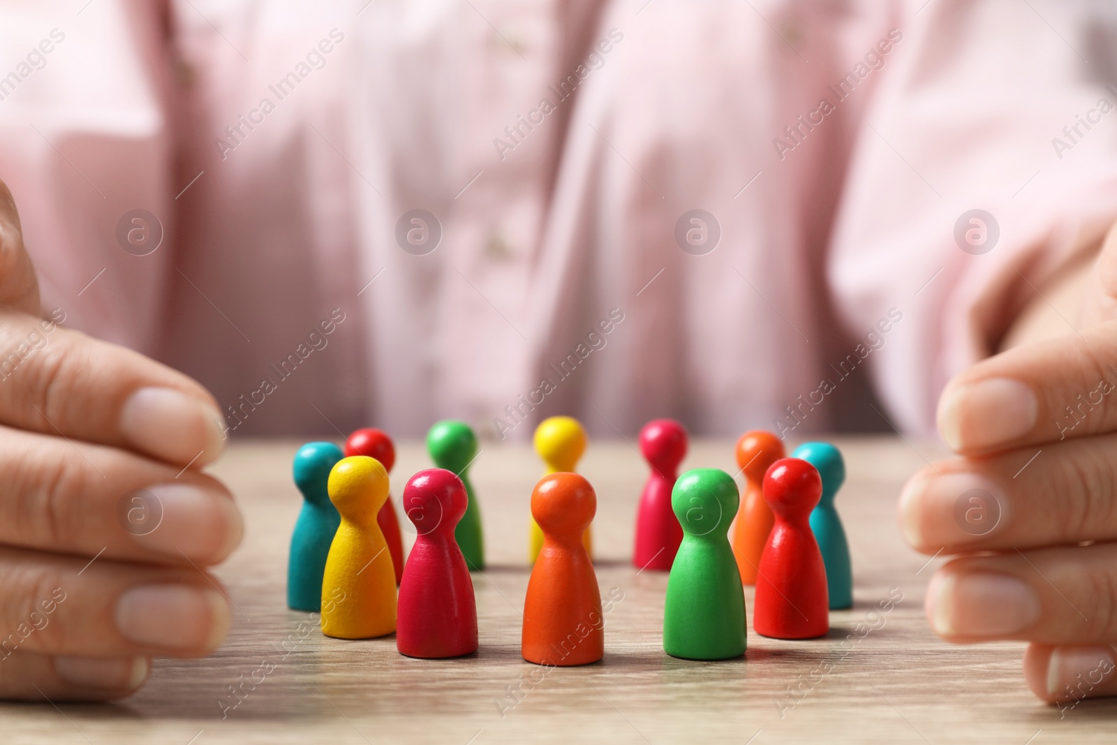 Photo of Woman protecting colorful pawns at wooden table, closeup. Social inclusion concept