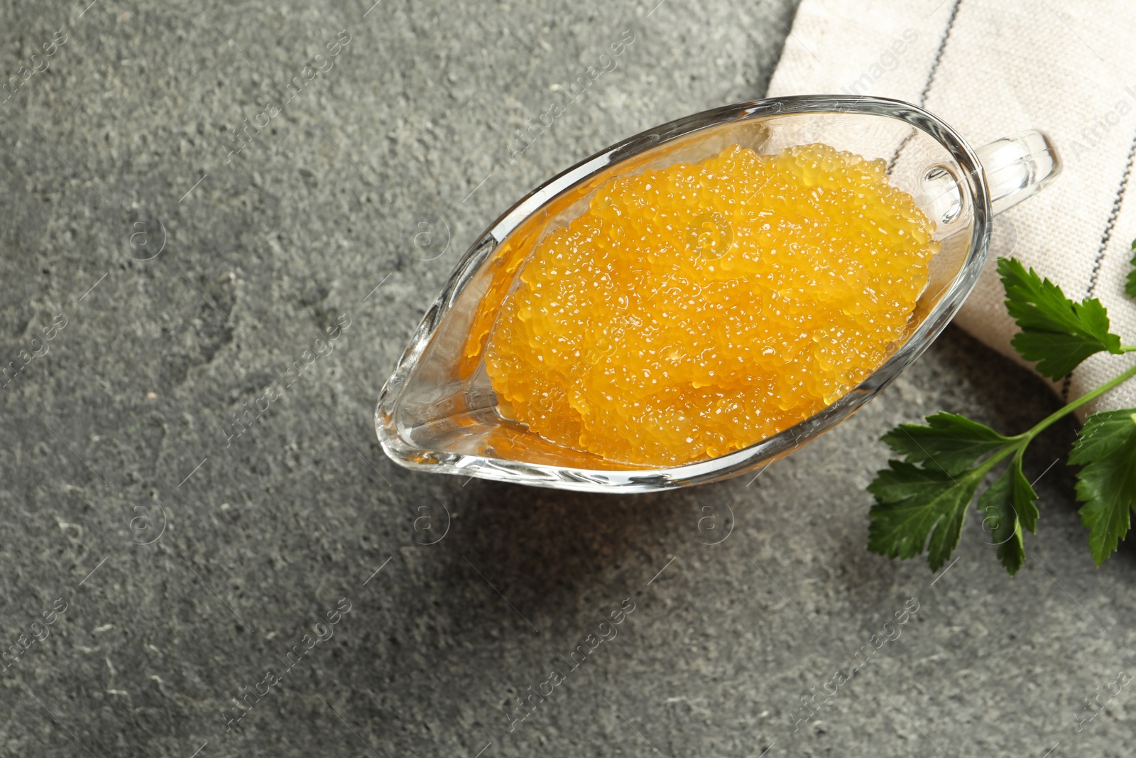 Photo of Fresh pike caviar in gravy boat and parsley on grey table, top view. Space for text