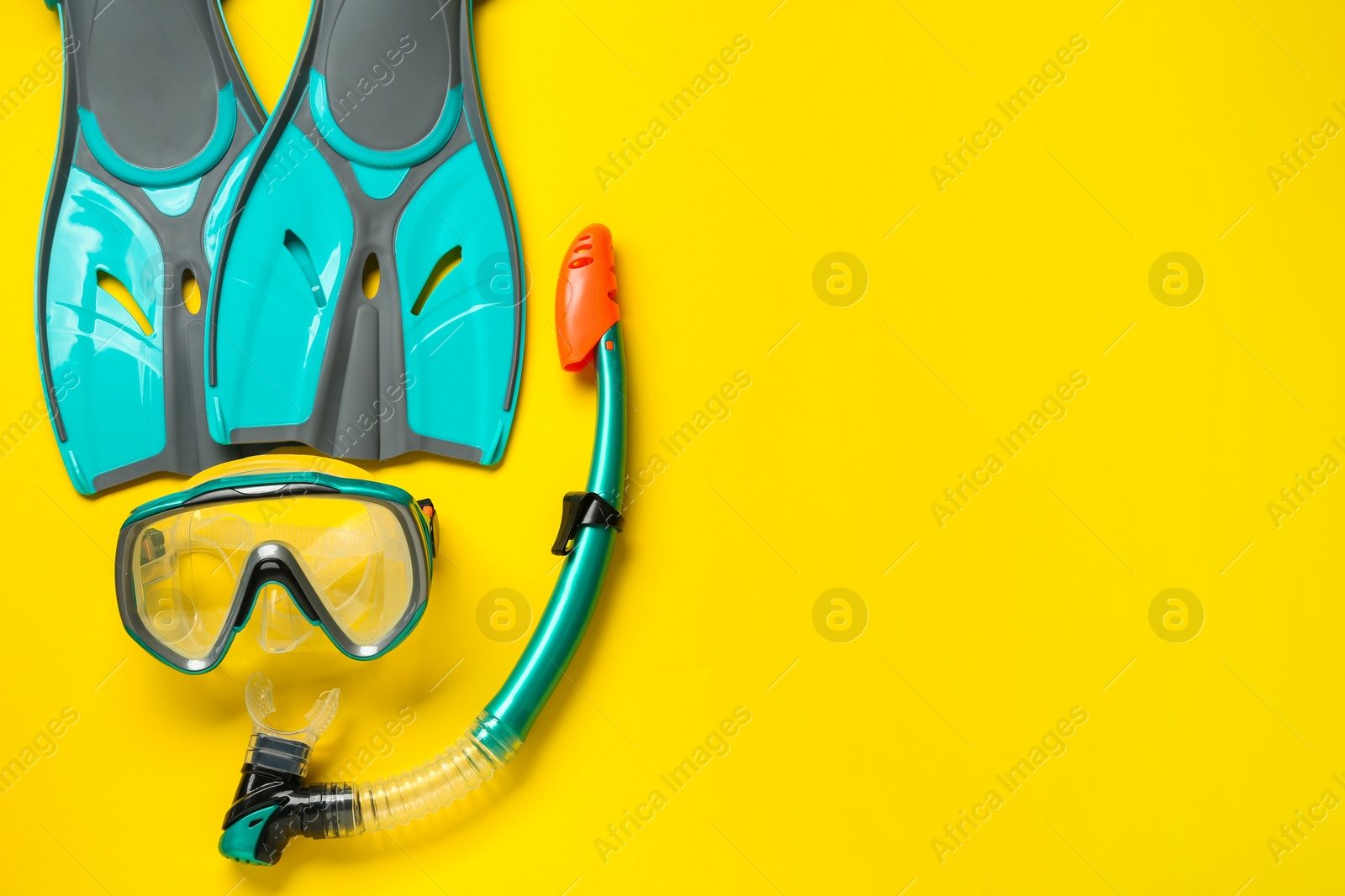 Photo of Pair of turquoise flippers and mask on yellow background, flat lay. Space for text