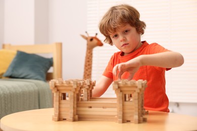 Photo of Little boy playing with wooden fortress at table in room. Child's toy