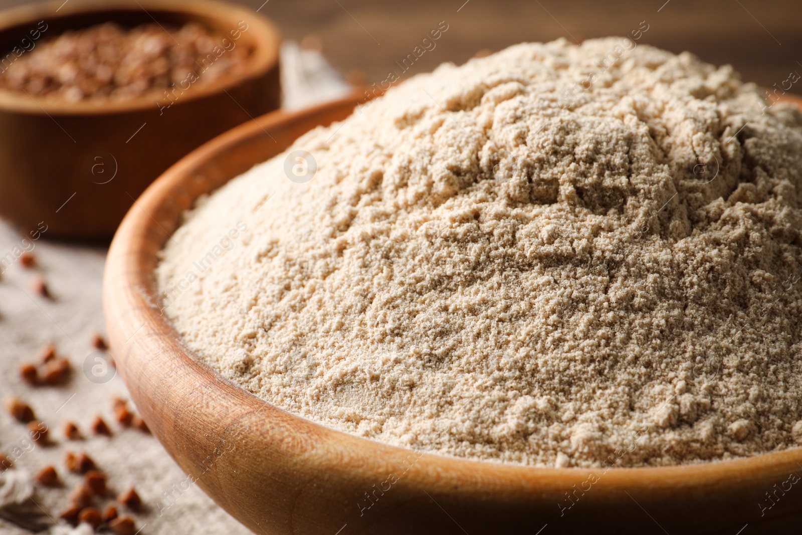 Photo of Bowl of buckwheat flour on wooden table, closeup