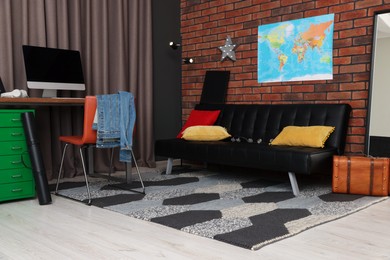 Stylish teenager's room with computer, black sofa and world map on brick wall