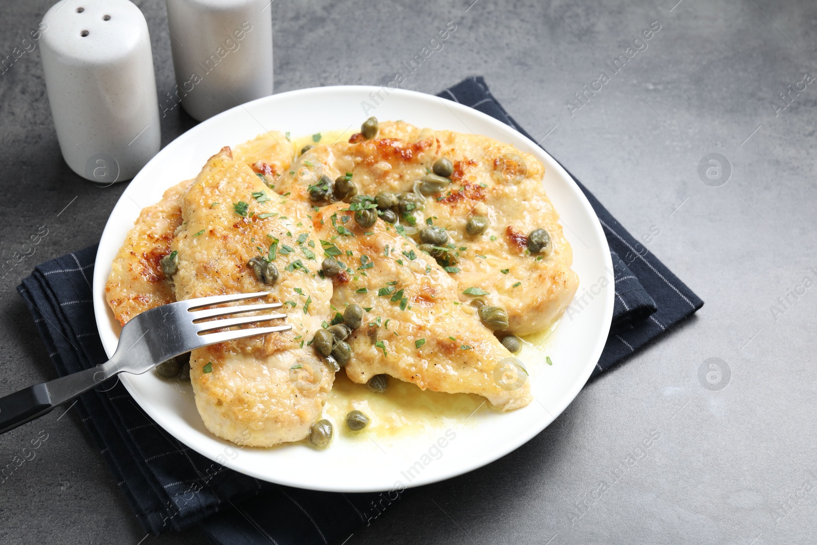 Photo of Delicious chicken piccata with herbs served on grey table