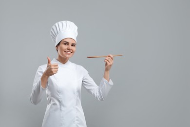 Happy female chef with wooden spoon showing thumbs up on light grey background. Space for text