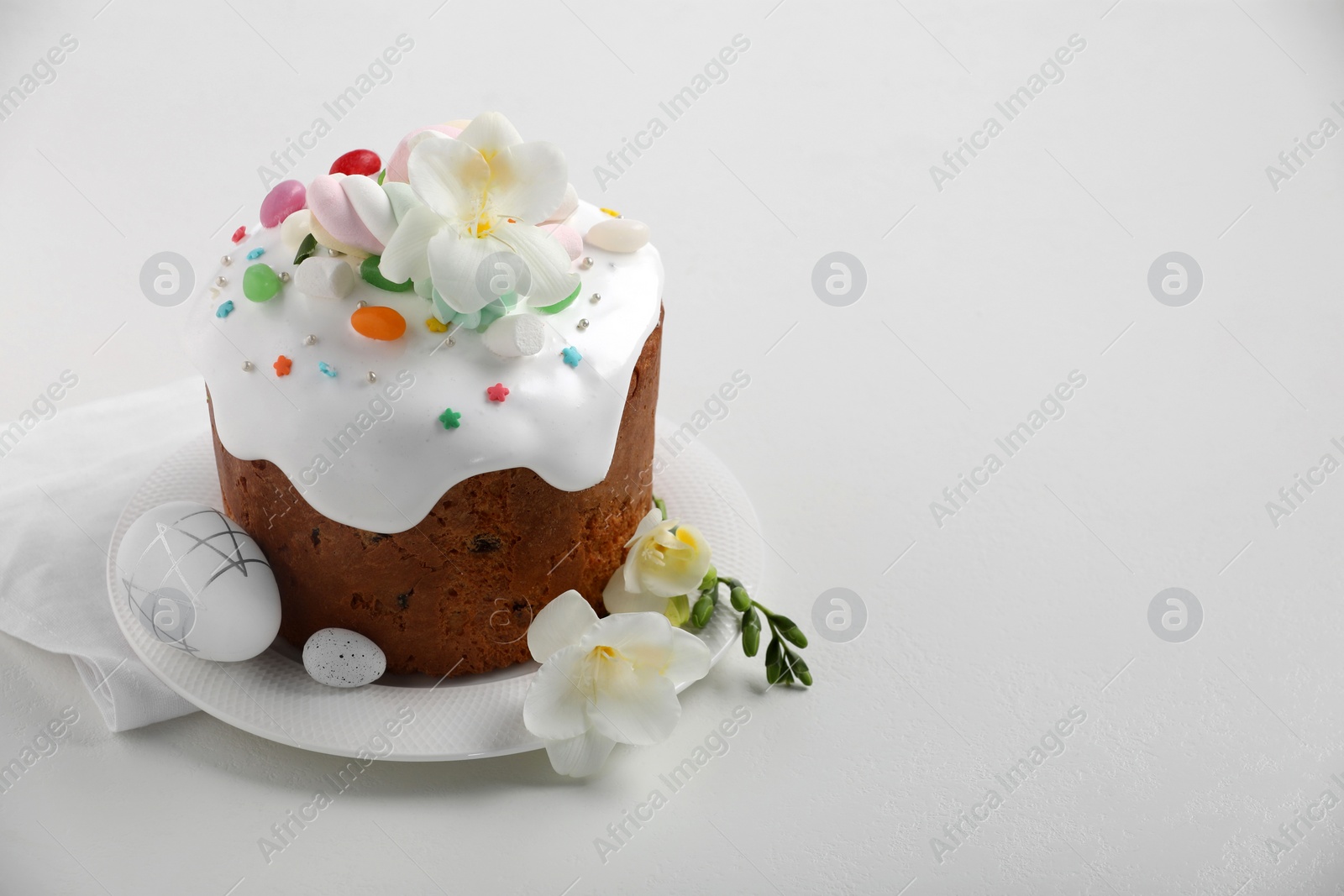 Photo of Traditional Easter cake with sprinkles, jelly beans, marshmallows, flowers and decorated eggs on white table, space for text