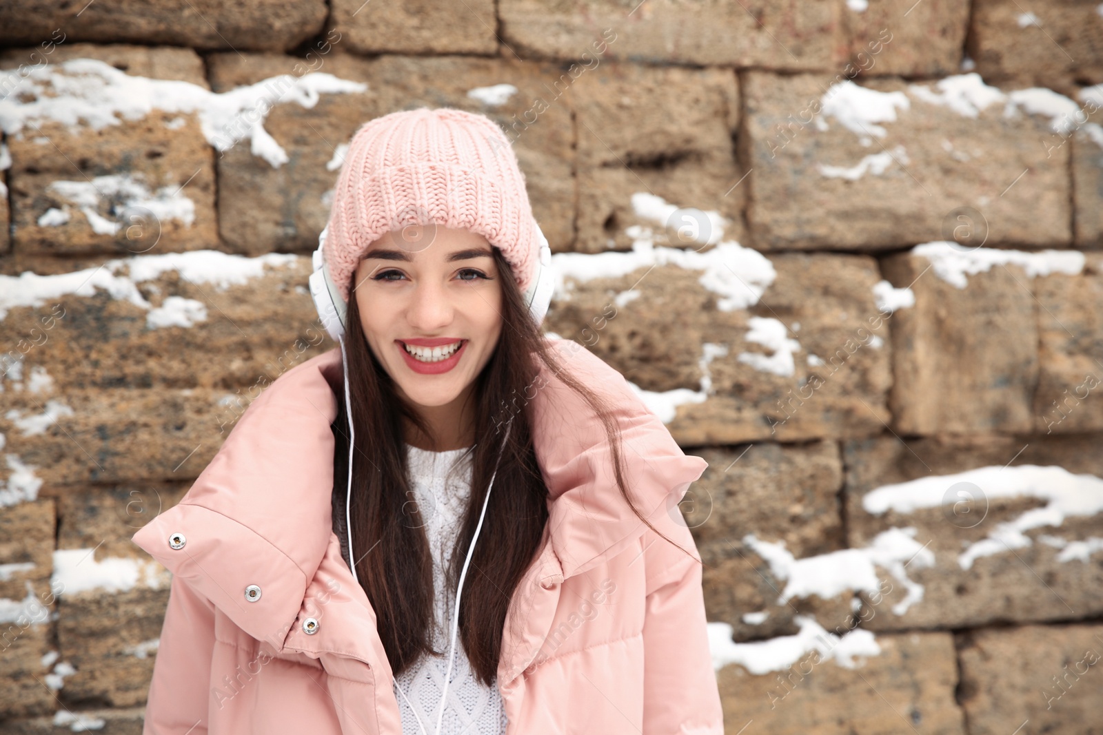 Photo of Young woman listening to music with headphones against stone wall. Space for text