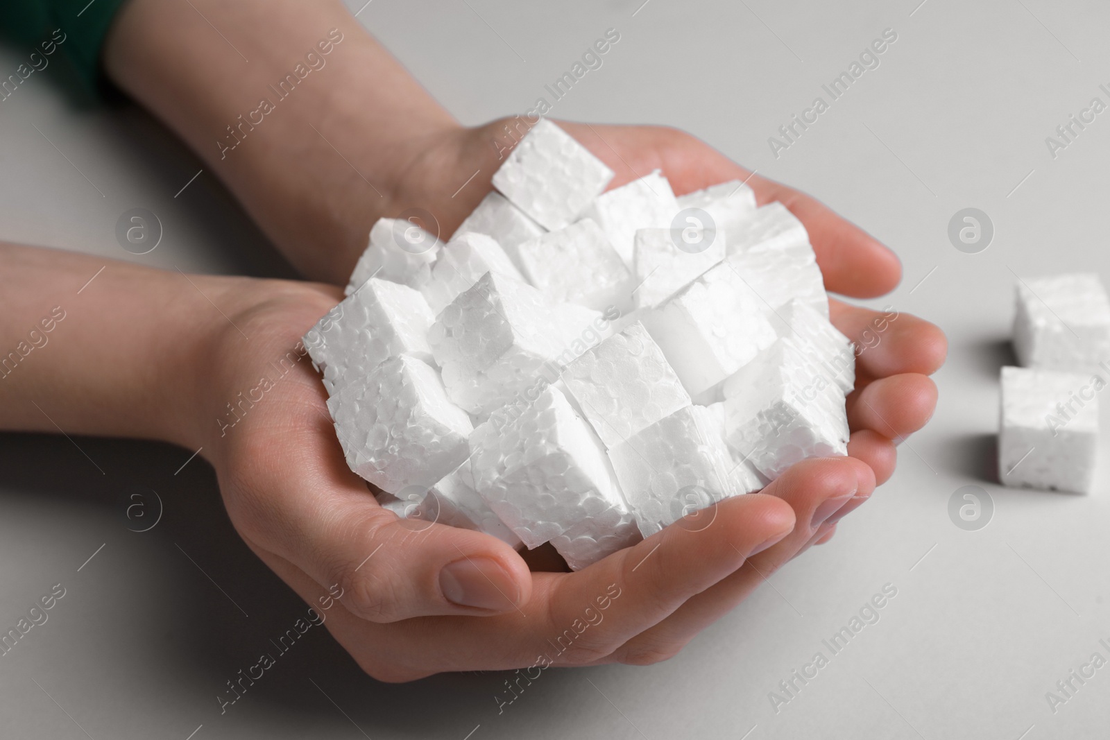 Photo of Woman with handful of styrofoam cubes on light grey background, closeup