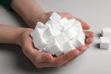 Photo of Woman with handful of styrofoam cubes on light grey background, closeup