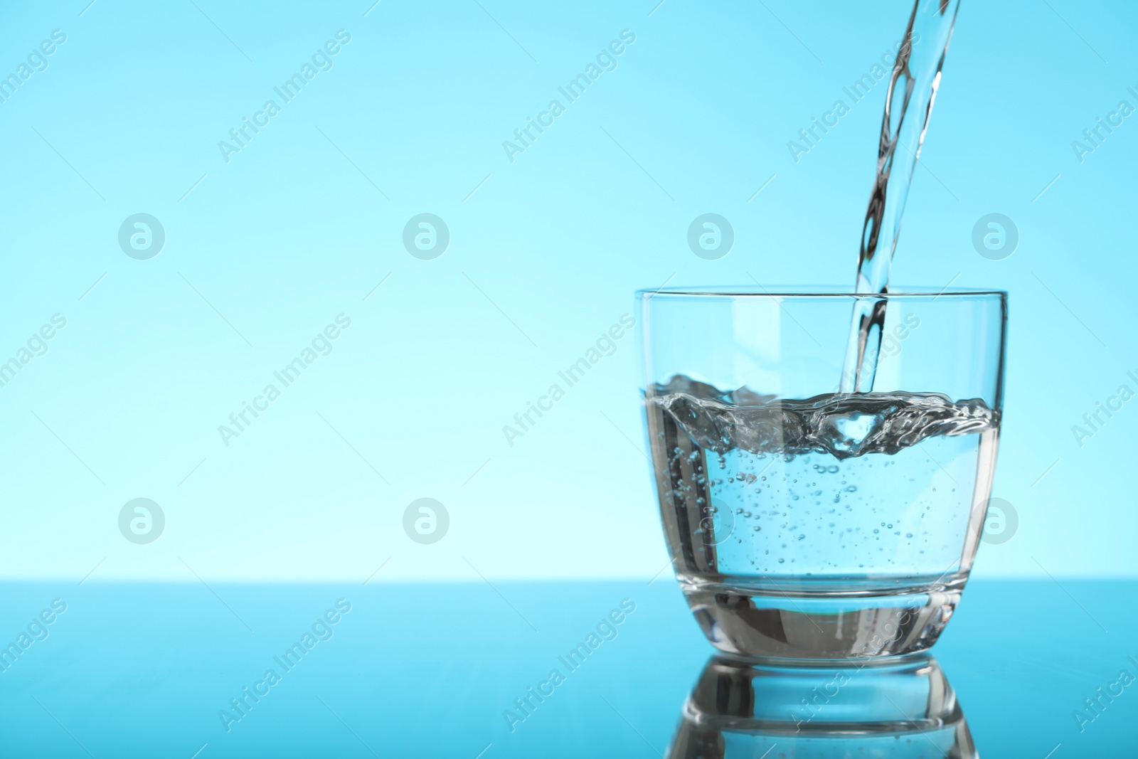 Photo of Pouring water into glass on blue background, space for text. Refreshing drink