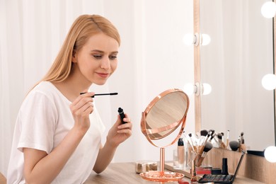 Beautiful woman applying makeup near mirror in room