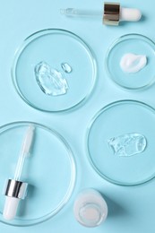 Petri dishes with samples of cosmetic serums, bottle and pipettes on light blue background, flat lay