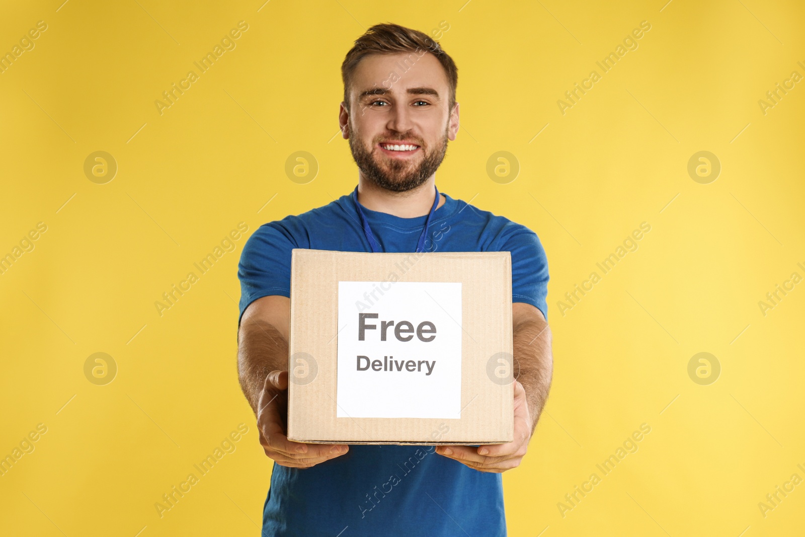 Photo of Male courier holding parcel with sticker Free Delivery on yellow background