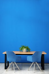 Modern table with potted fern near blue wall. Space for text