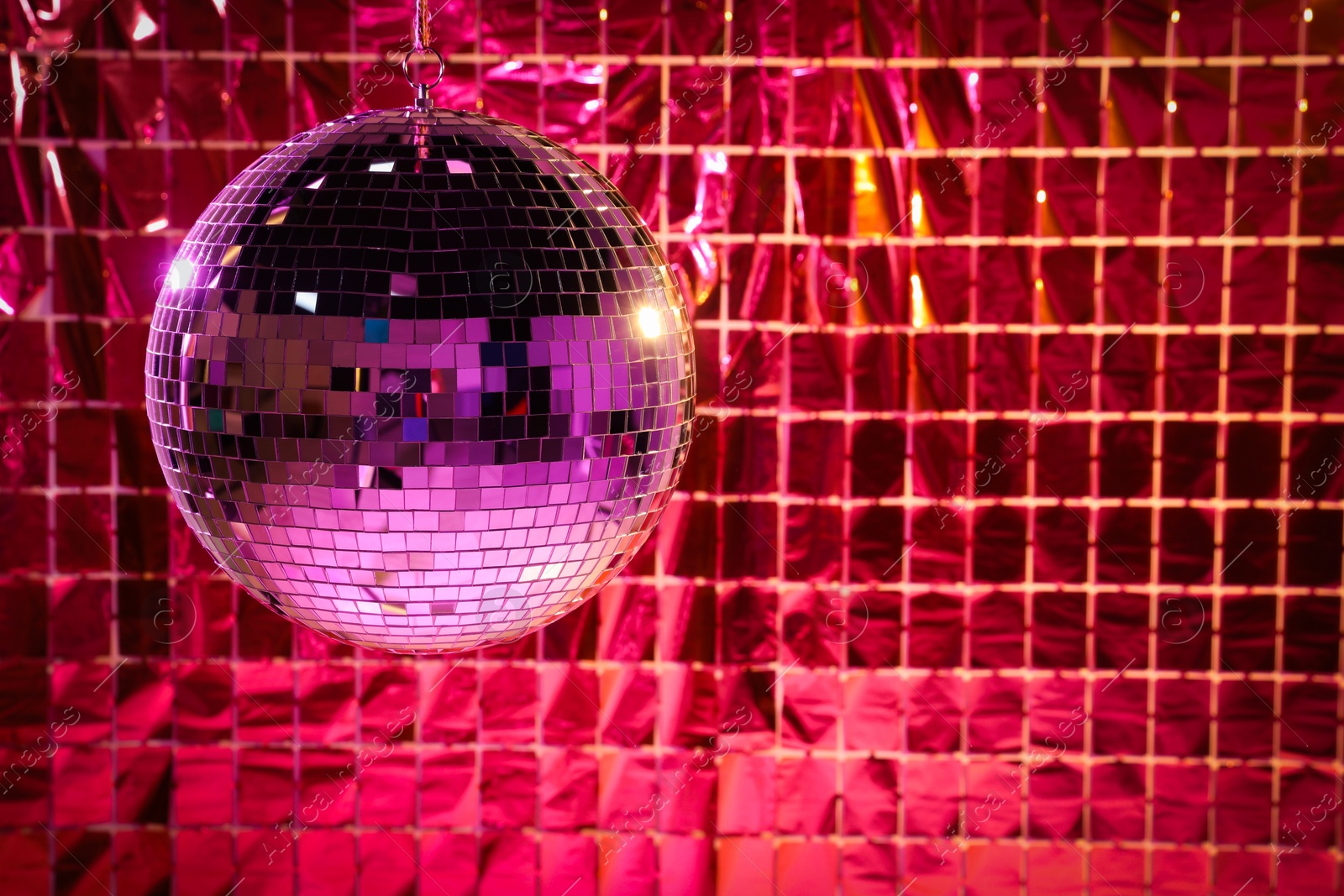 Photo of Shiny disco ball against foil party curtain under pink light, space for text