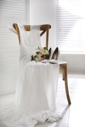 White high heel shoes, flowers and wedding dress on wooden chair indoors