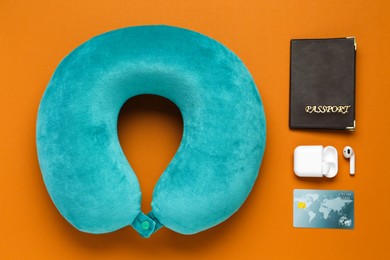 Photo of Turquoise travel pillow, passport, credit card and earphones on orange background, flat lay