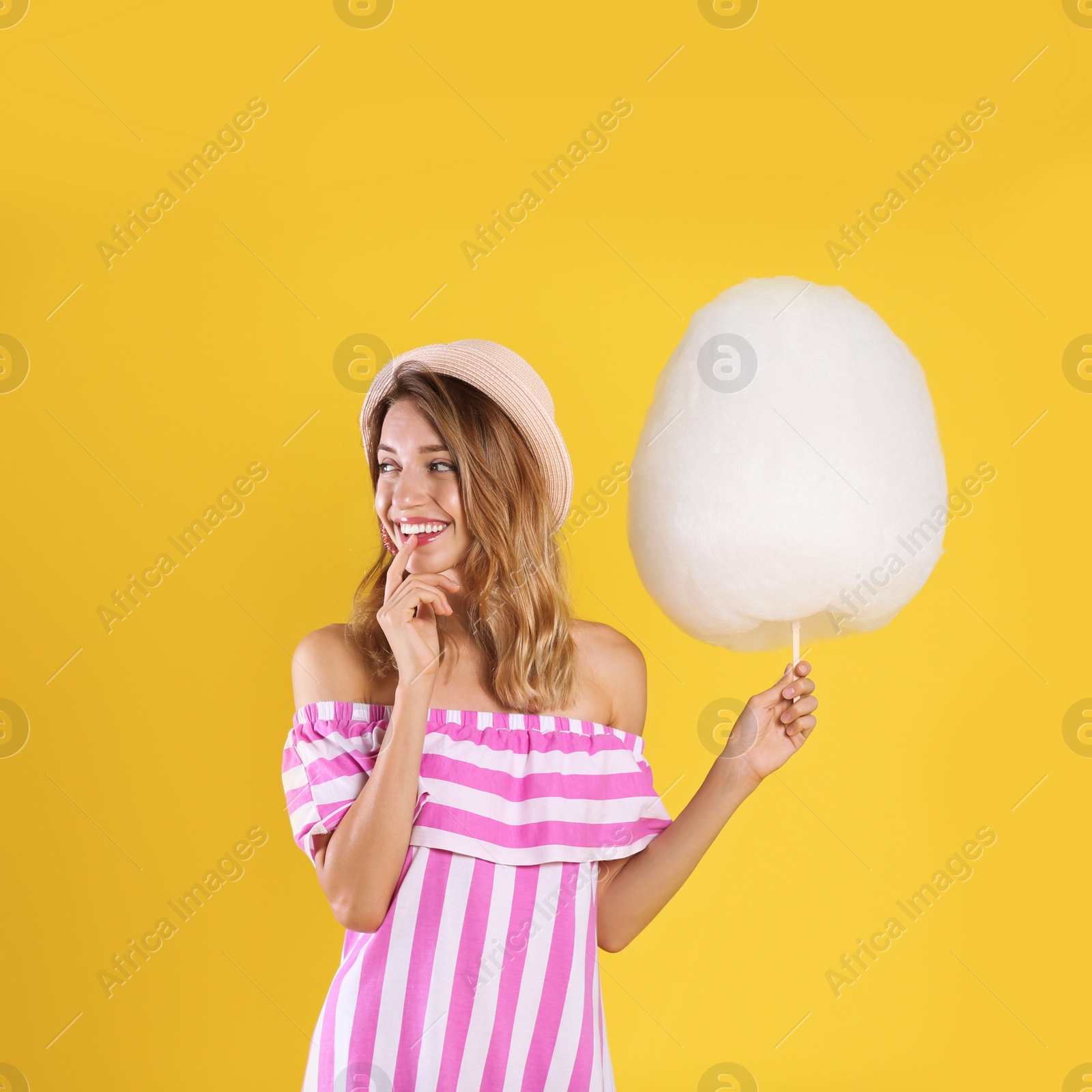 Photo of Happy young woman with cotton candy on yellow background