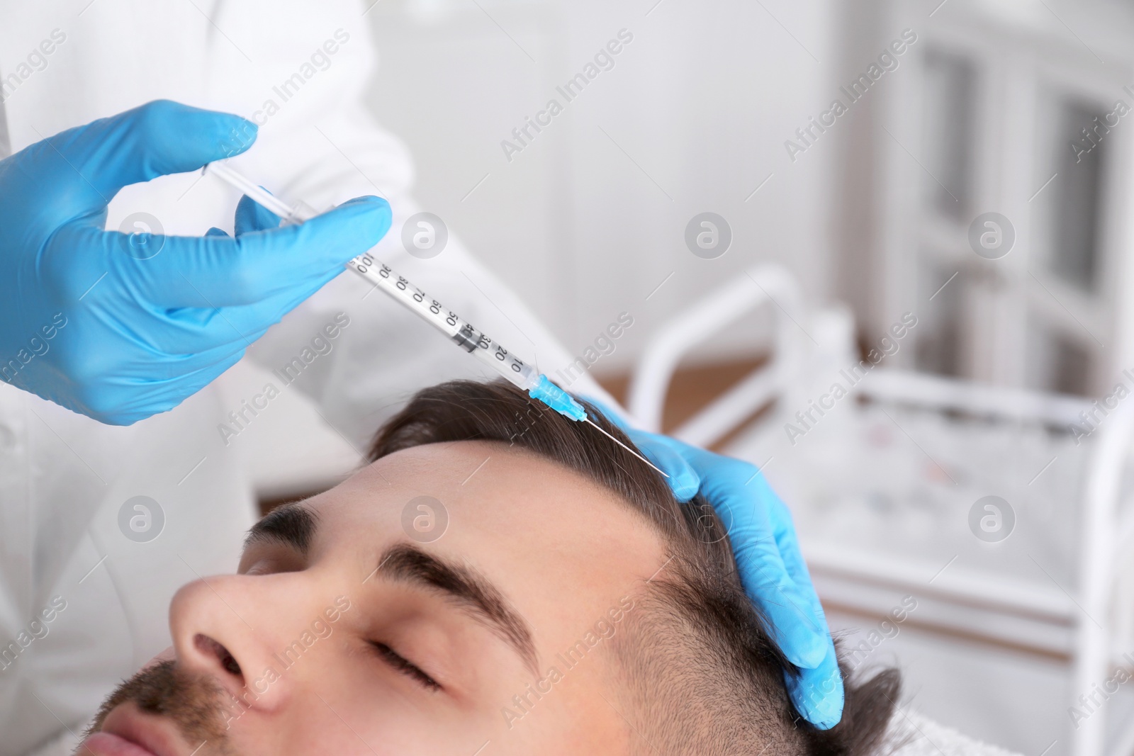 Photo of Young man with hair loss problem receiving injection in salon, closeup