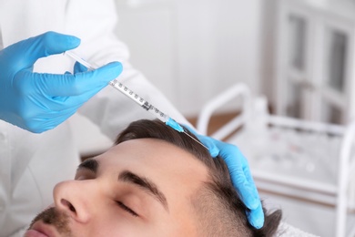 Young man with hair loss problem receiving injection in salon, closeup