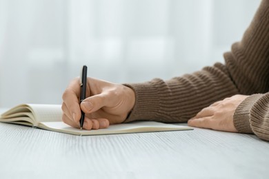 Man writing in notebook at white wooden table, closeup