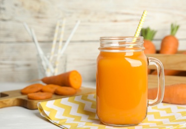 Freshly made carrot juice in mason jar on white table, space for text