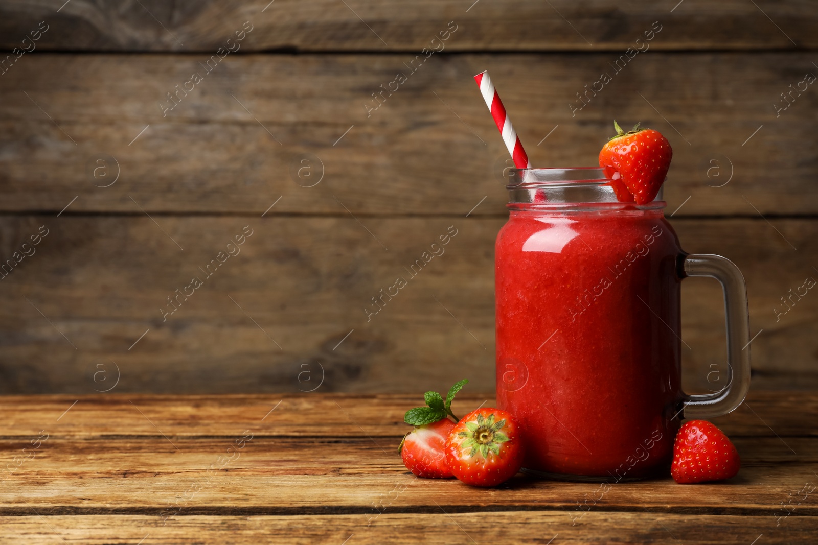 Photo of Mason jar with delicious strawberry smoothie and fresh berries on wooden table. Space for text