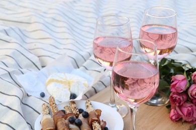 Photo of Glasses of delicious rose wine, flowers and food on white picnic blanket