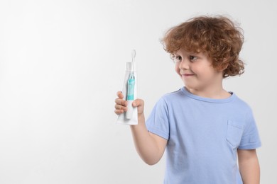 Photo of Cute little boy holding electric toothbrush and tube of toothpaste on white background, space for text