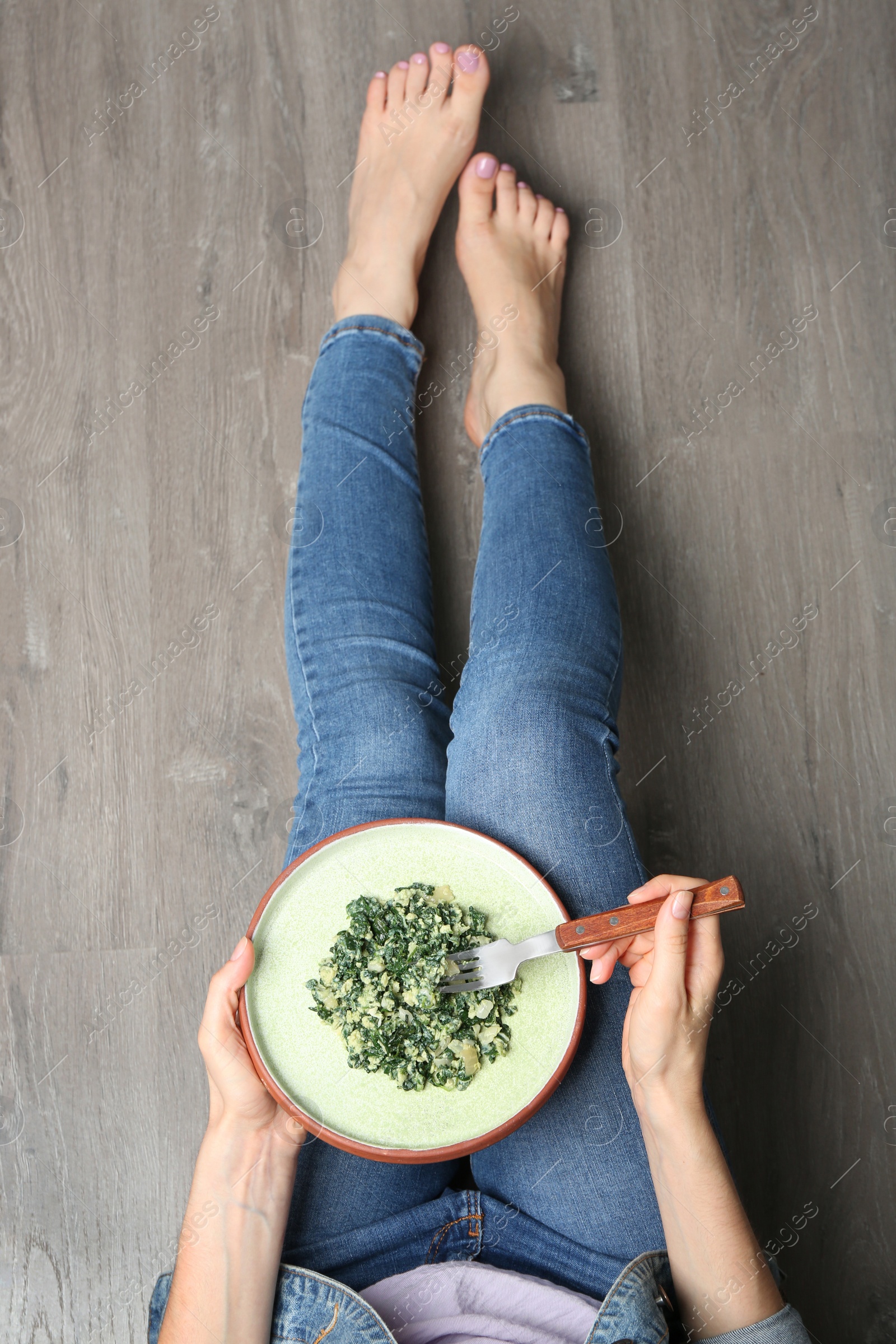 Photo of Young woman with tasty cooked spinach on wooden floor, top view. Healthy food