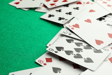 Photo of Scattered playing cards on green table, closeup. Space for text