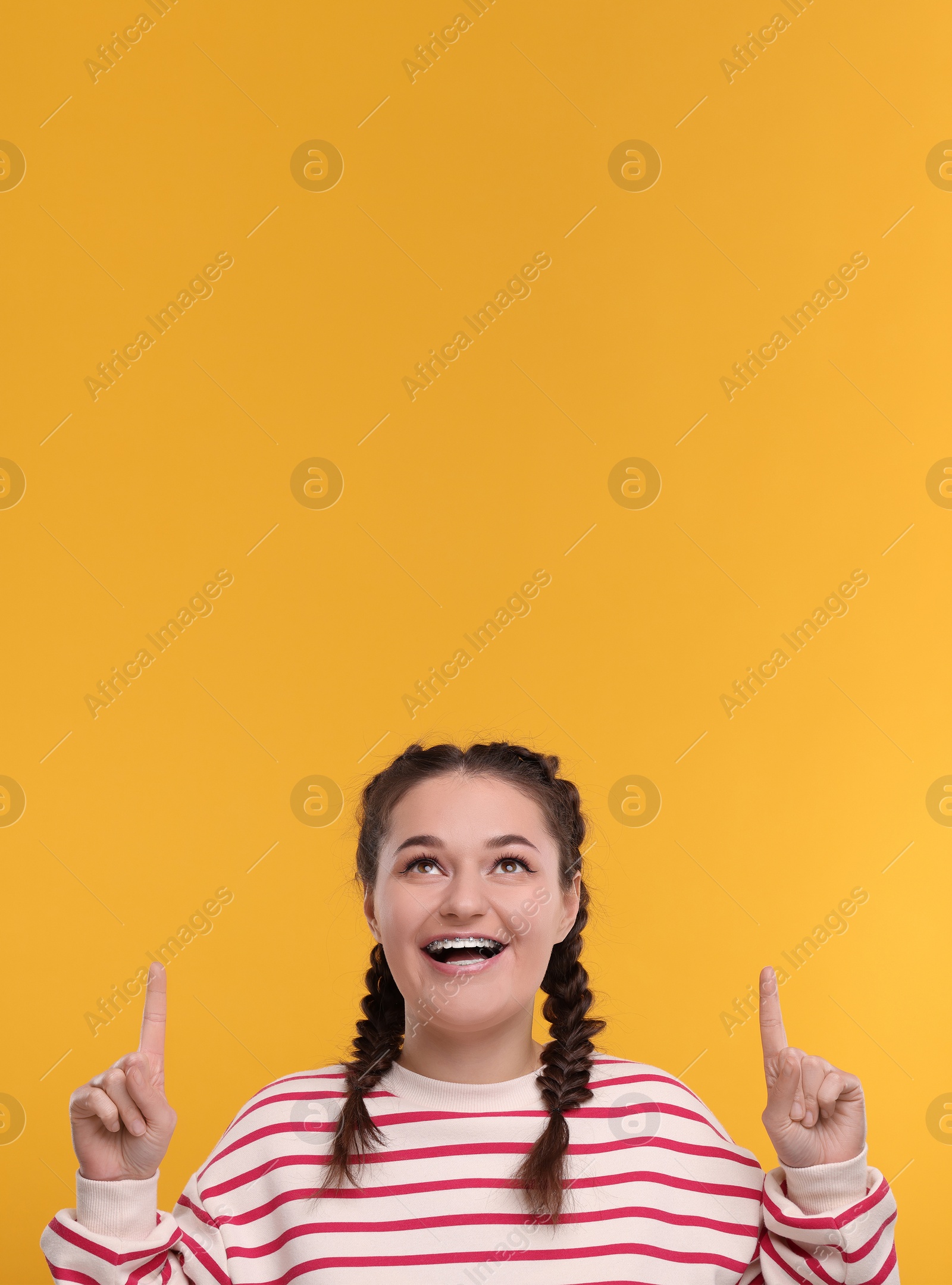 Image of Smiling woman with braces pointing at something on orange background. Space for text