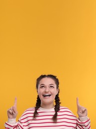 Image of Smiling woman with braces pointing at something on orange background. Space for text