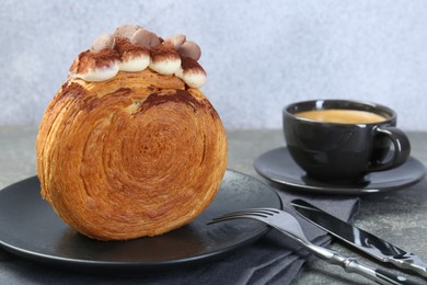 Photo of Round croissant with chocolate chips and cream served on grey table, closeup. Tasty puff pastry
