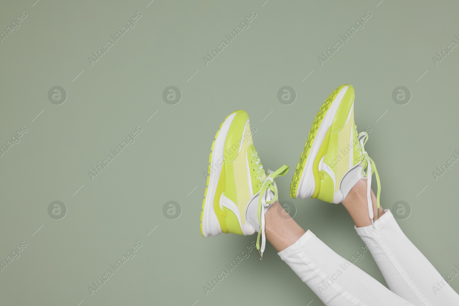 Photo of Woman wearing pair of new stylish sneakers on light green background, closeup. Space for text