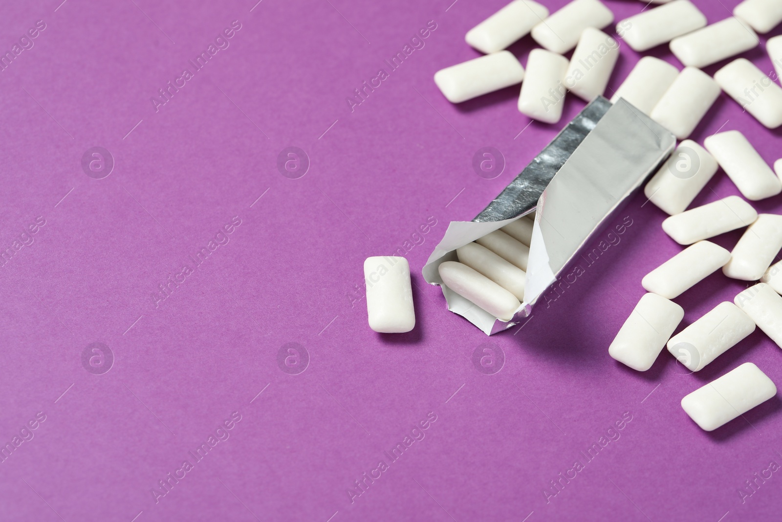 Photo of Pack with tasty chewing gums on purple background, space for text