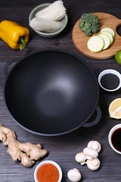 Photo of Empty iron wok and ingredients on dark grey wooden table, above view