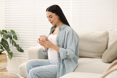 Pregnant woman with cup of drink on sofa at home