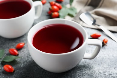 Photo of Fresh rose hip tea and berries on grey table, closeup