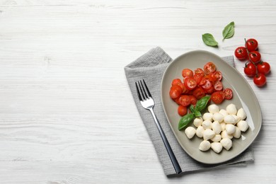 Photo of Delicious mozzarella balls, tomatoes and fork on white wooden table, flat lay. Space for text