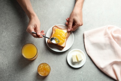 Photo of Woman spreading jam on toast bread at table, top view