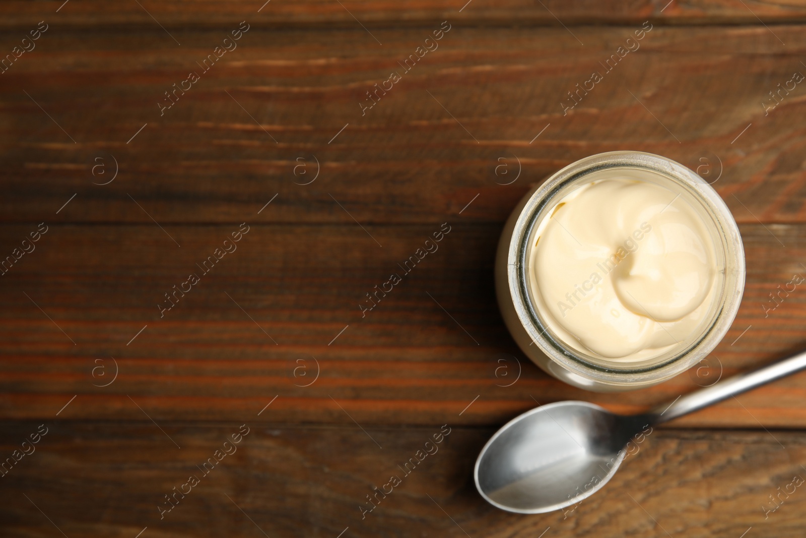 Photo of Jar of delicious mayonnaise and spoon on wooden table, flat lay. Space for text