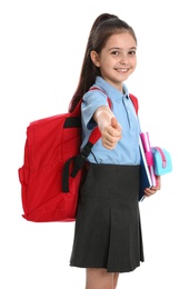 Photo of Cute little girl in school uniform with backpack and stationery showing thumbs-up on white background