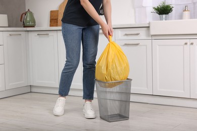 Photo of Woman taking garbage bag out of trash bin in kitchen, closeup