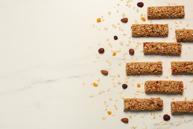 Photo of Tasty granola bars and ingredients on white marble table, flat lay. Space for text